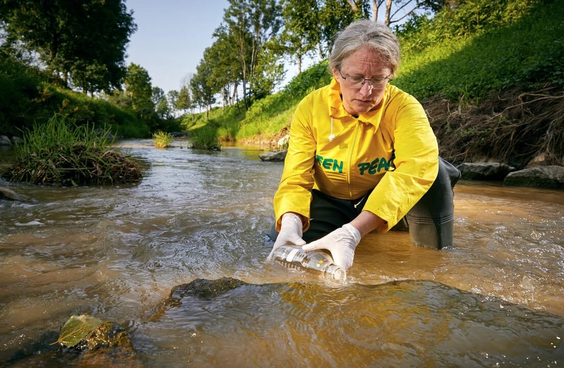 Attivista di Greenpeace preleva campioni d'acqua da un fiume vicino a uno dei più grandi allevamenti intensivi di suini a Schwarzaubach, in Austria.